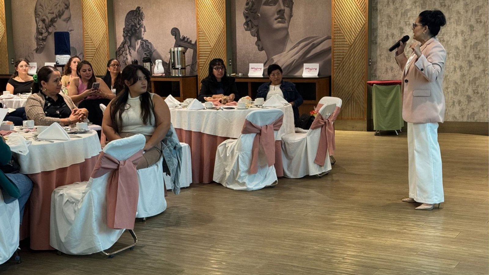 Miriam Rivera con micrófono, dando una conferencia frente a un grupo de mujeres